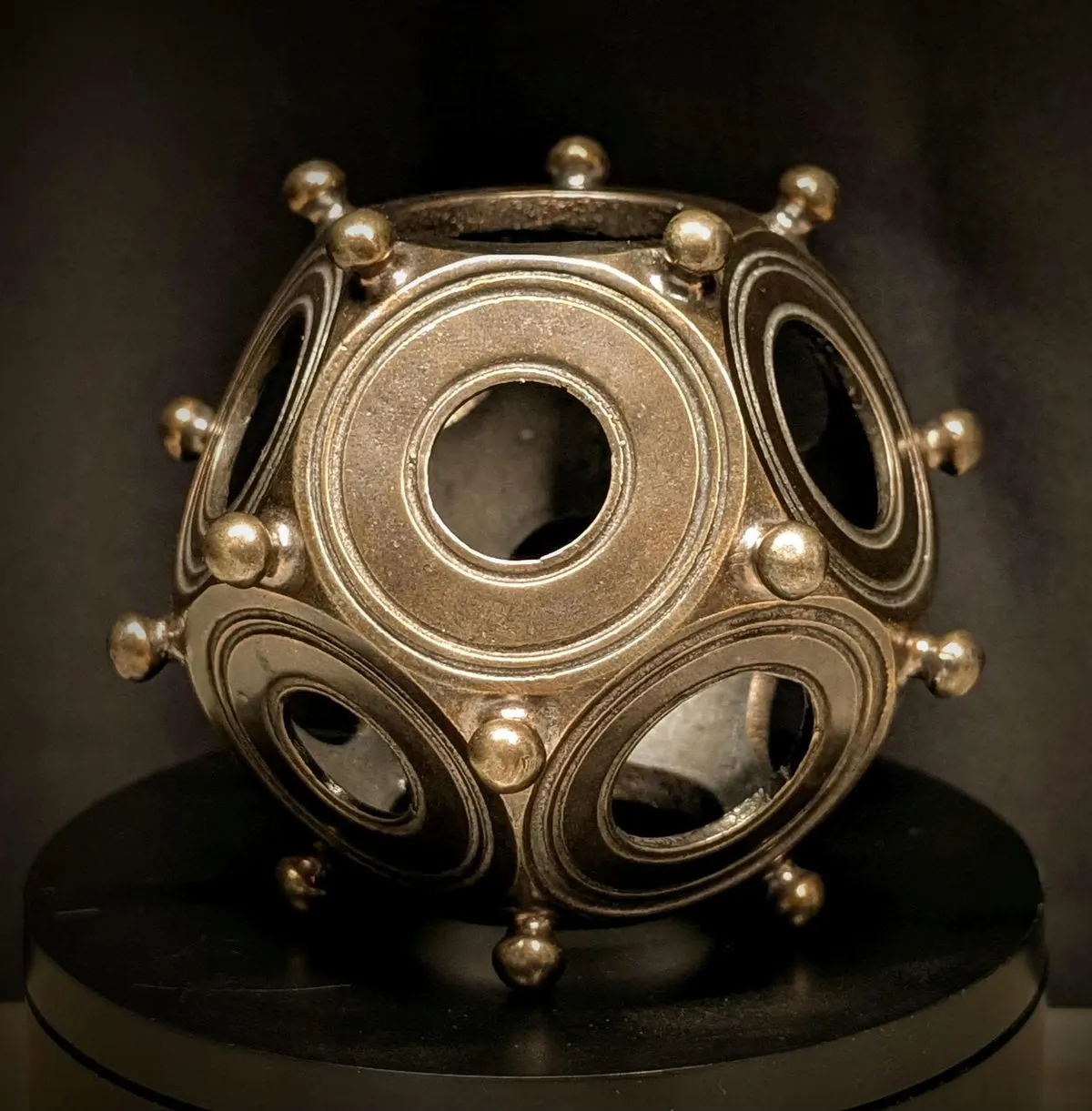 Solid metal Roman dodecahedron replica on a black stand